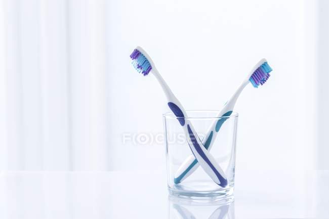 Cepillos de dientes morados en vidrio sobre fondo liso . - foto de stock
