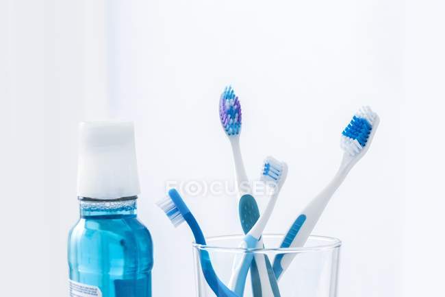 Cepillos de dientes en vidrio con enjuague bucal sobre fondo liso . - foto de stock
