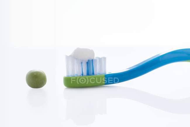 Cepillo de dientes con cantidad de pasta de dientes del tamaño de un guisante contra fondo blanco . - foto de stock