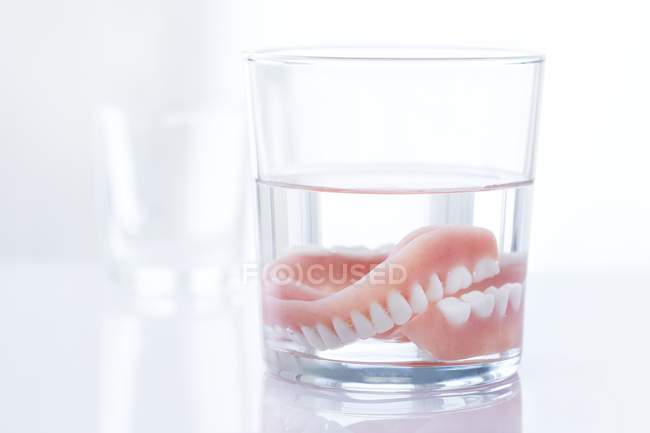 Prótesis dentales en vaso de agua sobre fondo blanco
. - foto de stock
