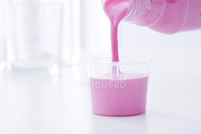 Medicamento rosa antiácido vertiendo en la taza de dosificación . - foto de stock