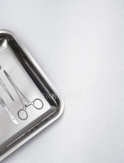 Chirurgische Schere und Werkzeug auf Tablett vor grauem Hintergrund. — Stockfoto