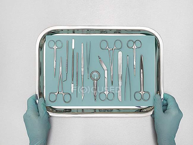 Medico mani che tengono vassoio con attrezzature chirurgiche su sfondo bianco . — Foto stock