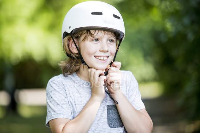 Junge befestigt Fahrradhelm im Park und lächelt. — Stockfoto
