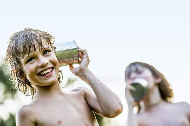 Shirtless boys playing with tin can telephone in park — Stock Photo