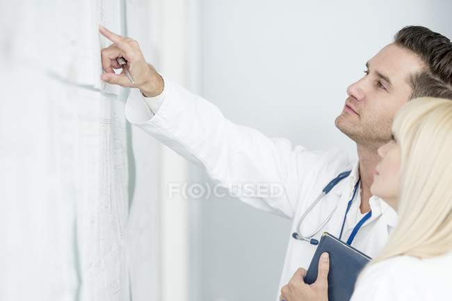Side view of male and female doctors inspecting white board. — Stock Photo