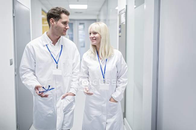 Male and female doctors in white coats walking down corridor. — Stock Photo