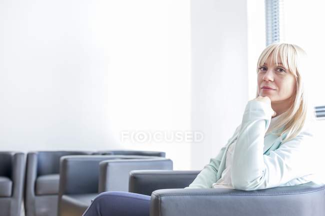 Pensiva donna adulta di mezza età seduta in sala d'attesa clinica con mano sul mento . — Foto stock