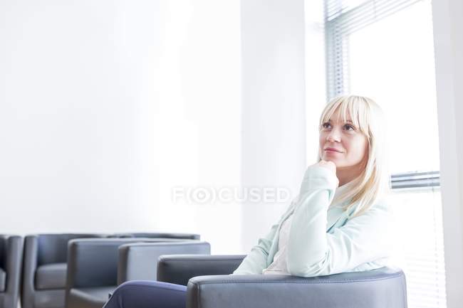 Pensiva mulher adulta média sentada na sala de espera clínica com a mão no queixo . — Fotografia de Stock