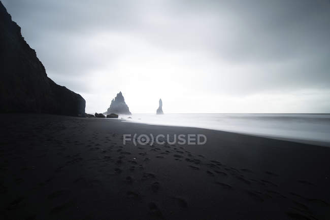 Felsformationen und Fußabdrücke auf Sand am Ufer in der Dämmerung bei reynisdrangar, vik, Island. — Stockfoto