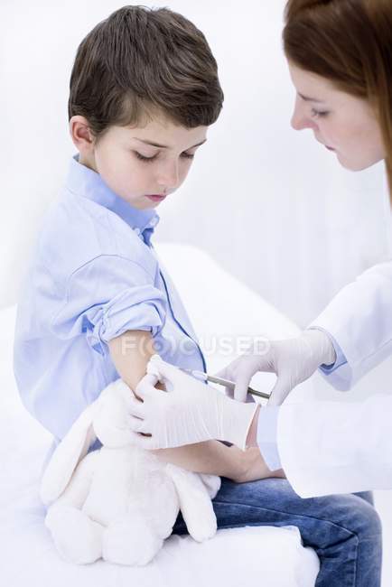 Doctor giving boy injection in arm in medical clinic. — Stock Photo