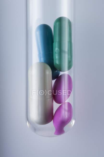 Comprimidos e cápsulas em tubo de ensaio sobre fundo cinzento . — Fotografia de Stock