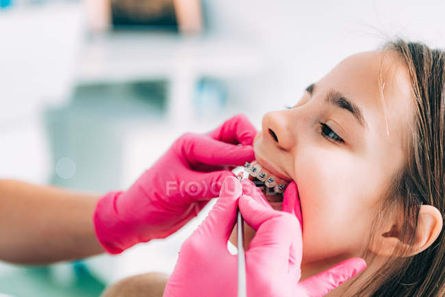 Ortodoncista femenina arreglando frenos dentales de niña en la clínica . - foto de stock