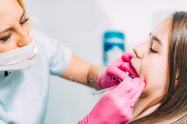 Ortodontista feminina que fixa aparelho dentário de menina na clínica . — Fotografia de Stock