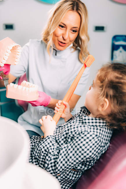 Bambina presso la clinica dentale imparare lavarsi i denti correttamente con ortodontista femminile . — Foto stock