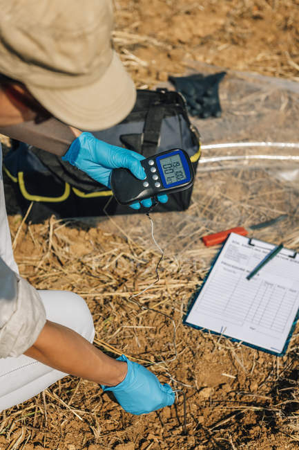 Female agronomist measuring soil temperature with thermometer in field. — Stock Photo