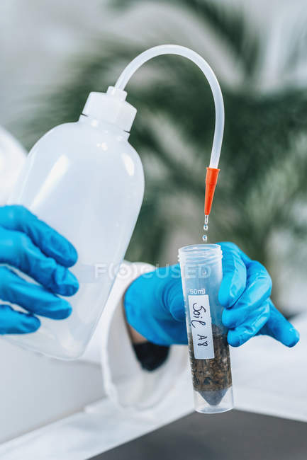 Bióloga hembra vertiendo agua en tubo de ensayo con muestras disueltas de suelo en laboratorio . - foto de stock