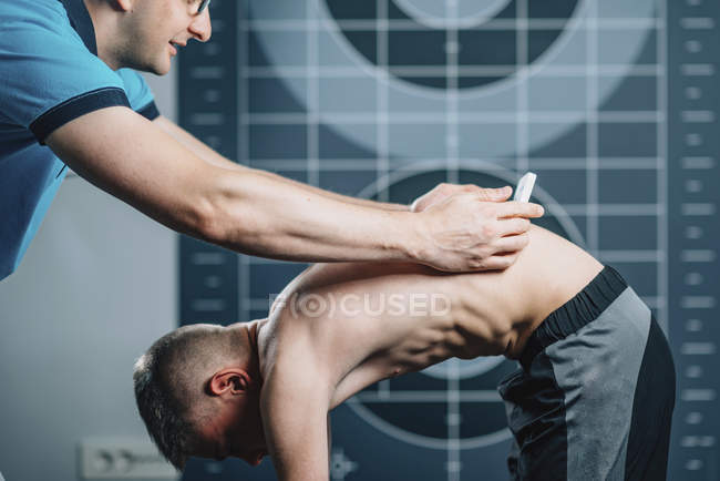 Инструктор-мужчина проводит скрининг сколиоза со сколиометром у подростка . — стоковое фото