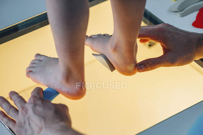 Physical therapist performing foot pressure scan for child on illuminated platform. — Stock Photo