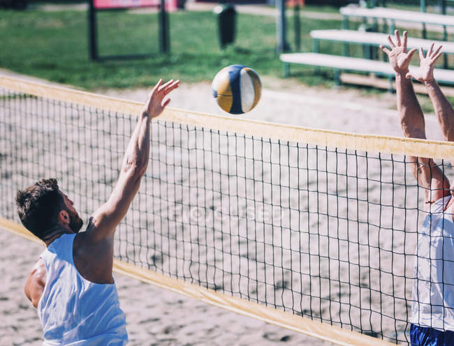 Jugadores de voleibol playa golpeando y bloqueando la pelota en la red mientras juego . - foto de stock