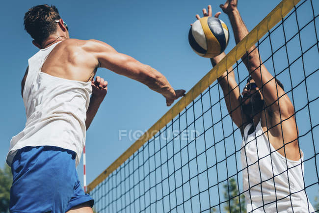 Low angle view of beach volleyball players hitting ball at net. — Stock Photo