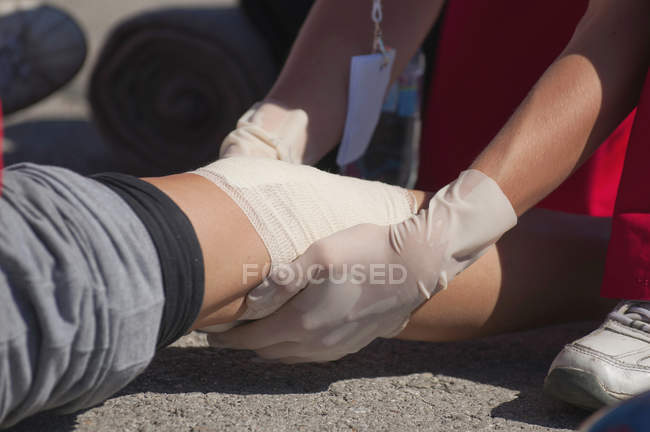 Nahaufnahme der Hände eines Sanitäters, der eine Knieverletzung mit einem Verband behandelt. — Stockfoto