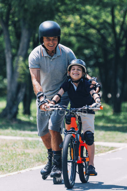 Grandfather and grandson riding together on roller skates and bicycle in park. — Stock Photo
