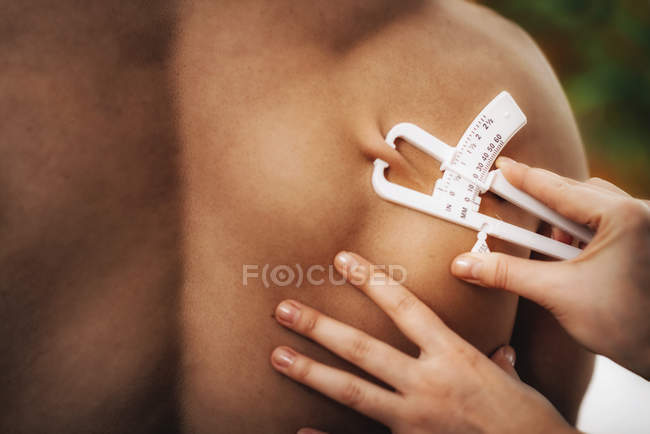 Médico que mide la grasa corporal en subescapular usando la prueba del espesor del pliegue cutáneo en atleta masculino
. - foto de stock