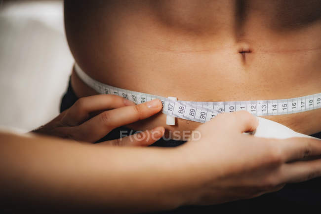 Médico que mide la circunferencia de la cintura con cinta métrica en atleta masculino . - foto de stock