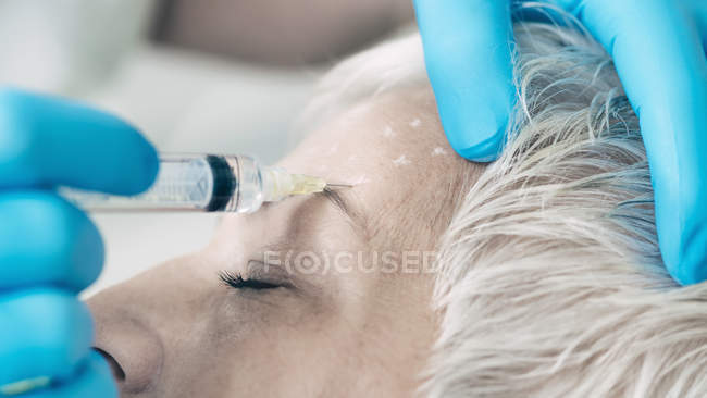 Mulher madura recebendo injeção de botox na testa na clínica de cosmetologia . — Fotografia de Stock
