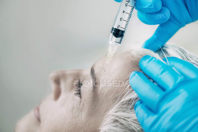Mujer madura que recibe inyección de botox en la frente en la clínica de cosmetología . - foto de stock