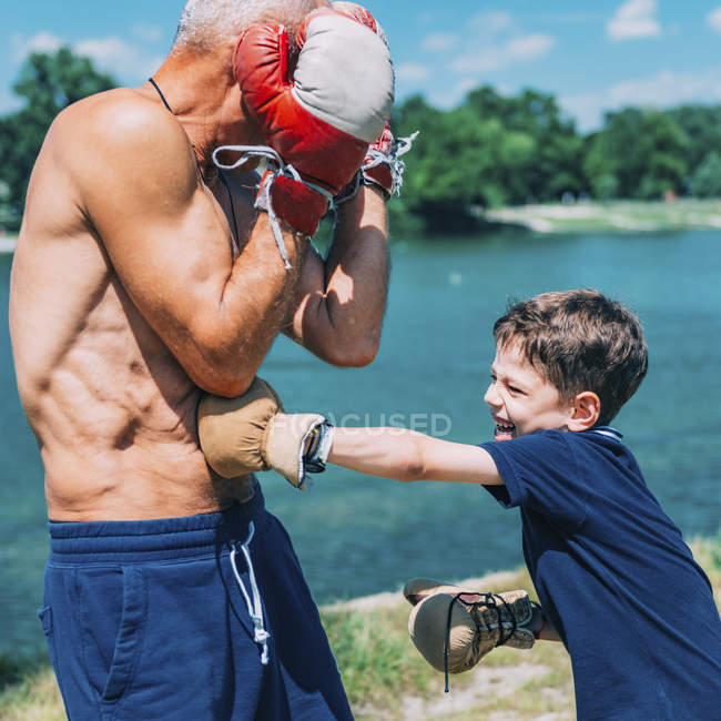 Abuelo y nieto boxeando junto al lago al aire libre . - foto de stock
