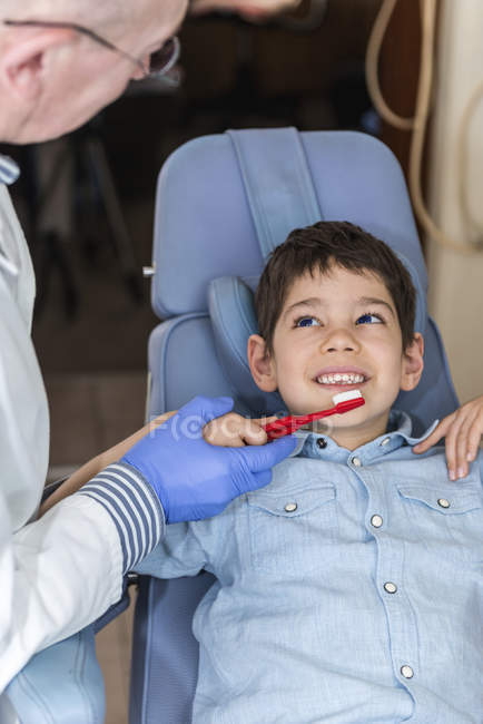 Dentista ensinando menino idade elementar sobre higiene dental com escova . — Fotografia de Stock