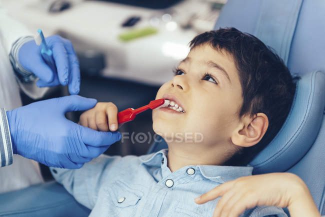 Dentista enseñando a niño de edad elemental sobre higiene dental con cepillo . - foto de stock