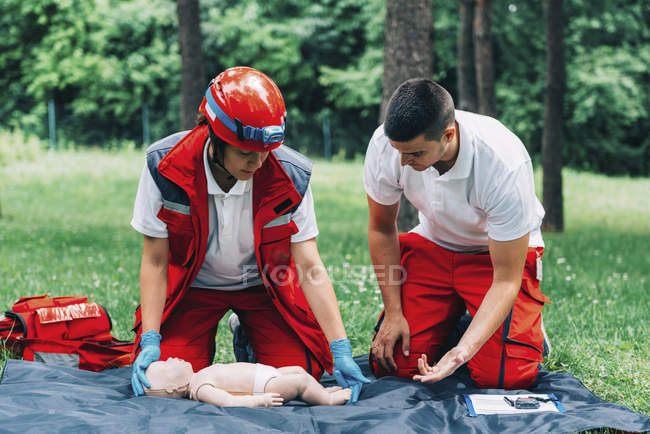 Female paramedic CPR training on baby dummy with instructor outdoors. — Stock Photo
