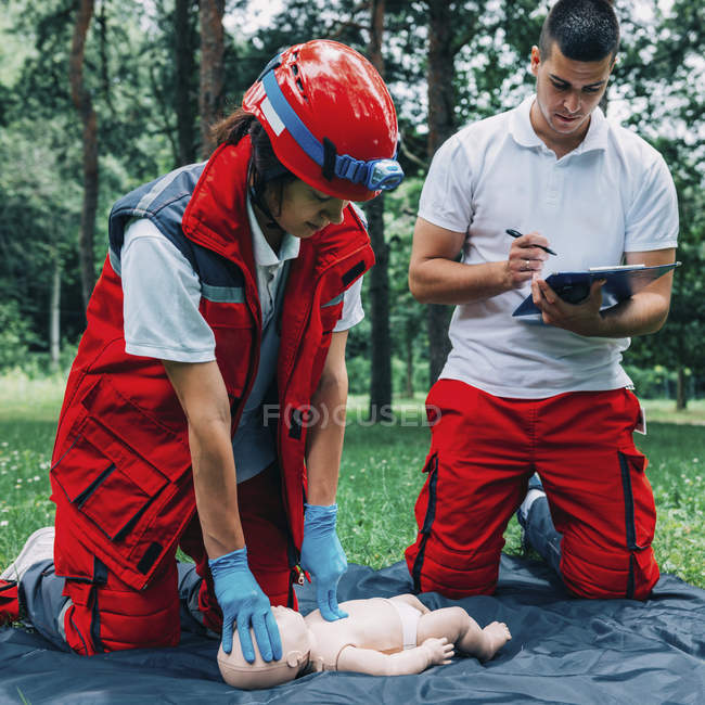 Female paramedic CPR training with instructor on baby dummy outdoors. — Stock Photo