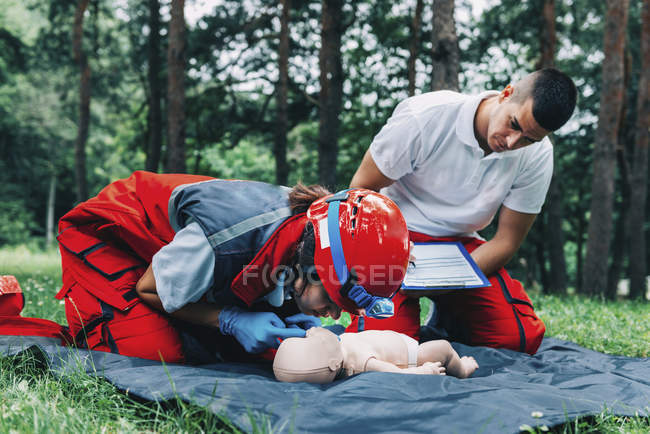 Female paramedic with instructor CPR training on baby dummy outdoors. — Stock Photo