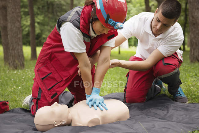 Female paramedic CPR training on dummy with instructor outdoors. — Stock Photo