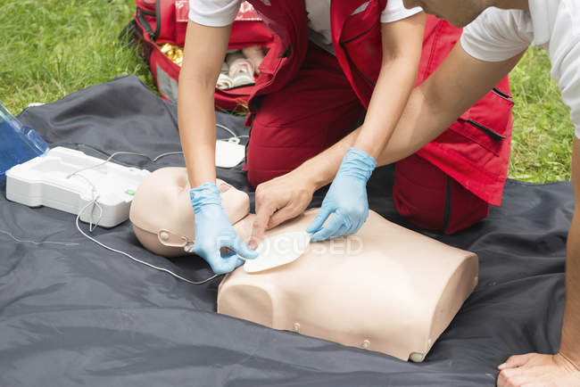 Un instructeur aide une ambulancière paramédicale à utiliser un défibrillateur à l'extérieur . — Photo de stock