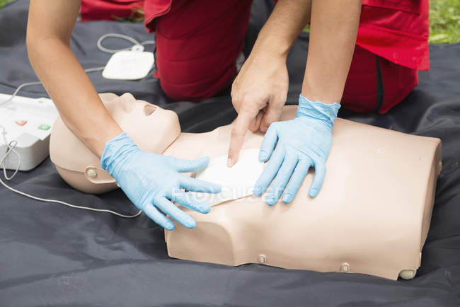 Un instructeur aide une ambulancière paramédicale à utiliser un défibrillateur à l'extérieur . — Photo de stock