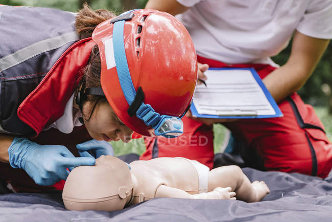 Treinamento de RCP paramédica feminina em boneco de bebê com instrutor ao ar livre . — Fotografia de Stock