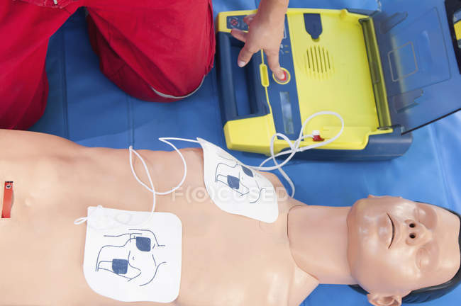 Défibrillateur portable activé par un ambulancier paramédical relié au mannequin de RCR pendant l'entraînement à la réanimation . — Photo de stock