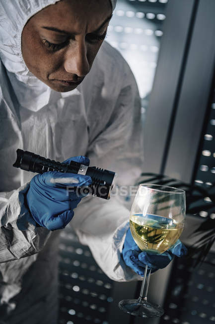 Forensics expert examining with flashlight evidence glass of wine at crime scene. — Stock Photo