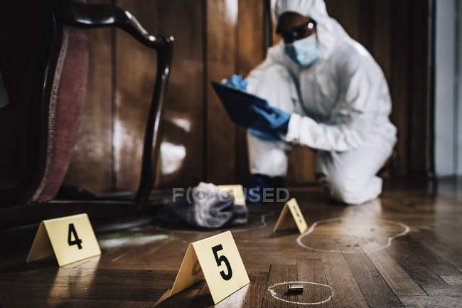 Perito forense em roupa protetora a escrever em prancheta a recolher provas da cena do crime
. — Fotografia de Stock