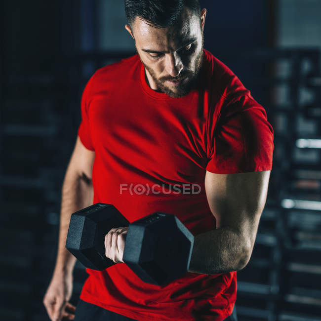 Young man exercising with dumbbell in gym. — Stock Photo