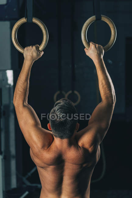 Hombre musculoso fuerte ejercitando en anillos gimnásticos . - foto de stock