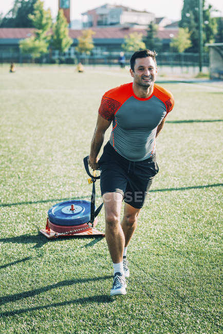 Man dragging sport tyre on green grass outdoors. — Stock Photo