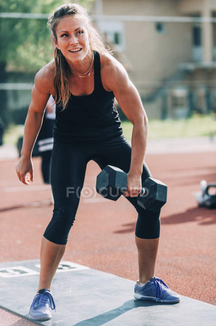 Жінка піднімає гантелі на легкоатлетичному стадіоні . — стокове фото