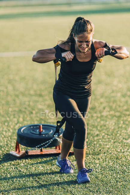 Woman dragging sport tyre on green grass outdoors. — Stock Photo