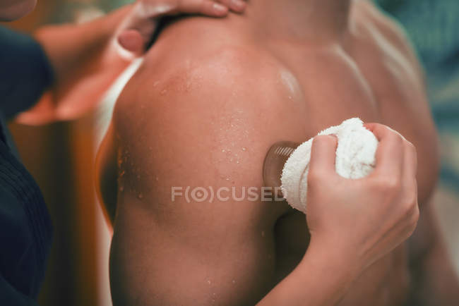 Fisioterapeuta femenina realizando criomasaje para el dolor de hombro . - foto de stock
